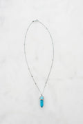 A silver chain necklace with a blue hexagonal crystal pendant on a white marble background.